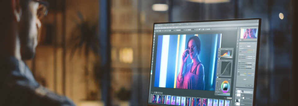Photographer editing a neon-lit portrait in photo enhancement software on a large monitor in a dark workspace