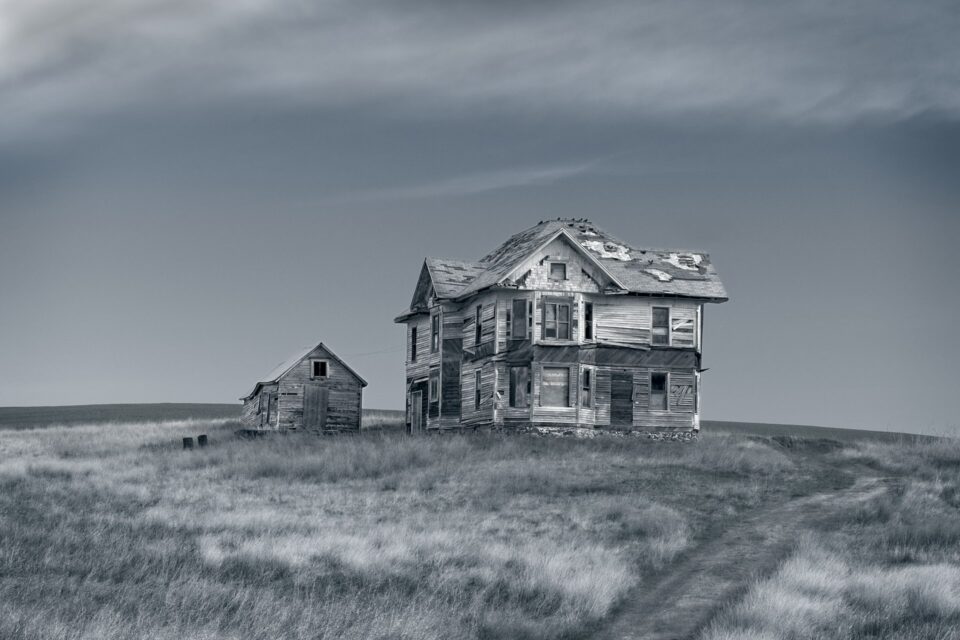 A weathered, two-story abandoned farmhouse sitting on a grassy hill in Rosalia, Washington, edited with a cinematic glow.