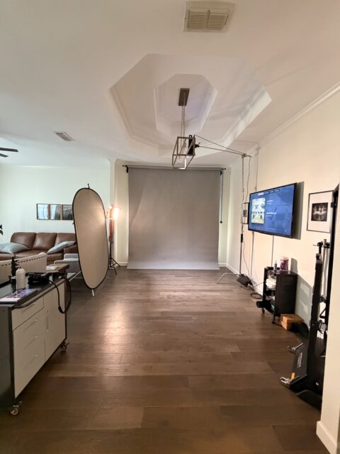 Home photo studio setup in a living room with gray seamless background and lighting gear