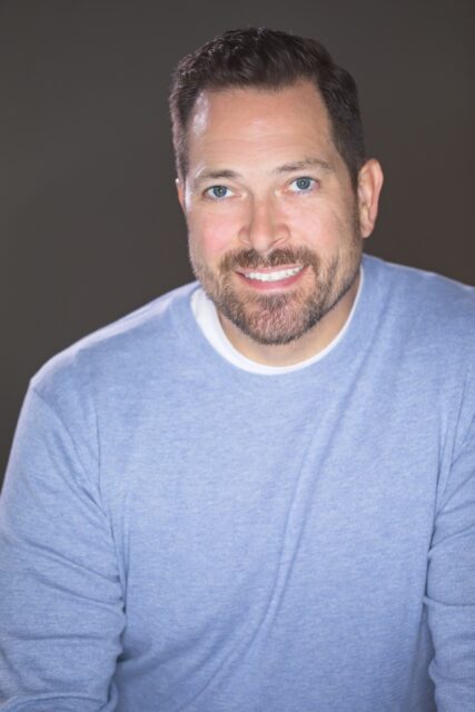 Self-portrait headshot photographed in a home studio against a gray background