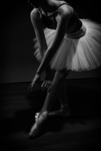 Black and white ballet dancer adjusting pointe shoe photographed in a home studio