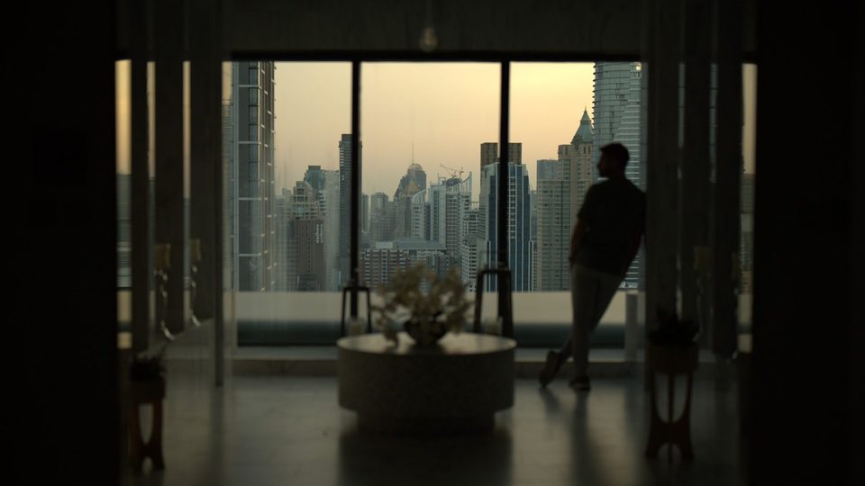 Man silhouetted at a window above a city skyline at dusk, before the Amber & Aqua LUT
